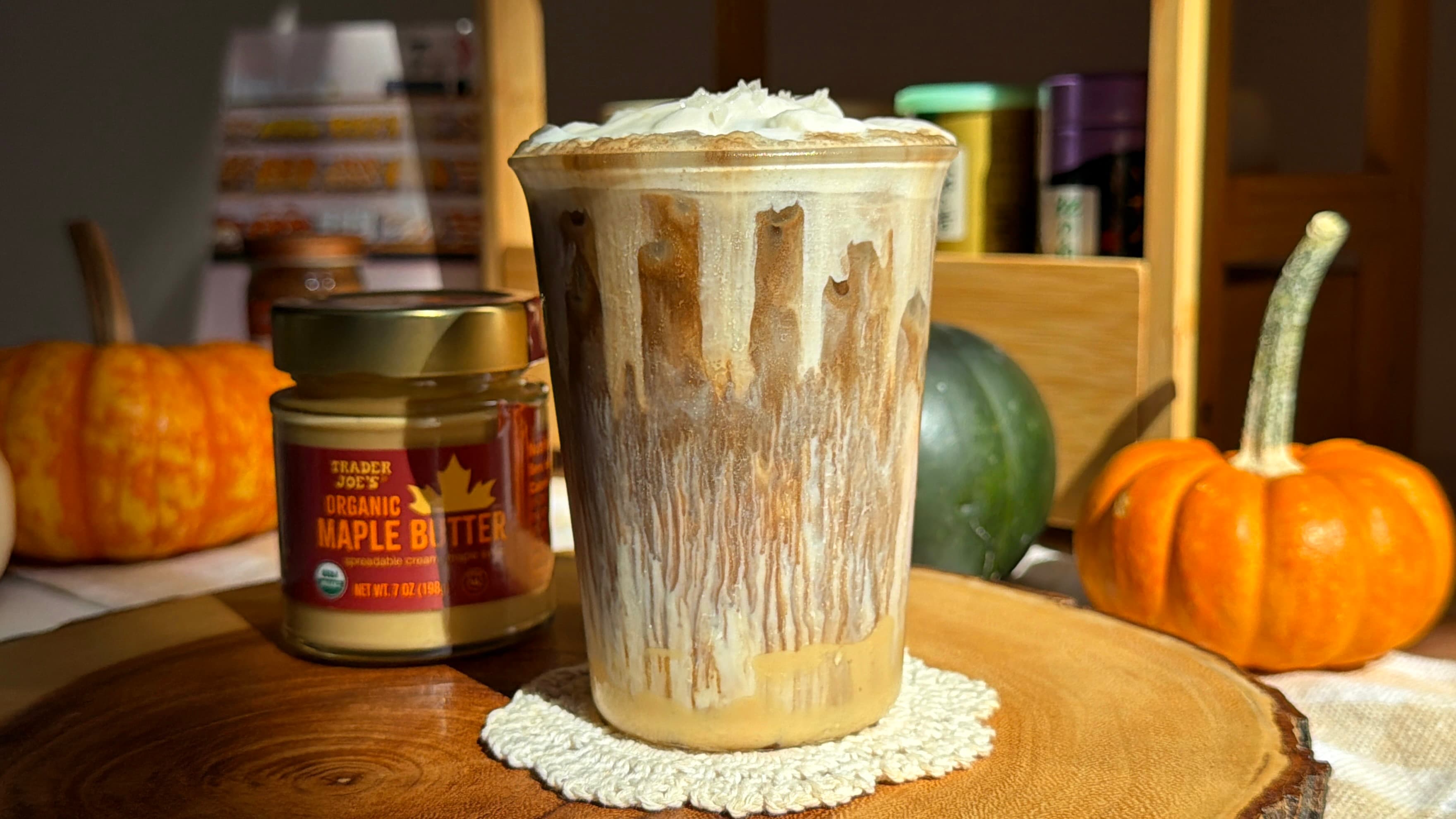 Iced hojicha latte with salted maple butter cream top, next to a jar of Trader Joe's organic maple butter and mini pumpkins