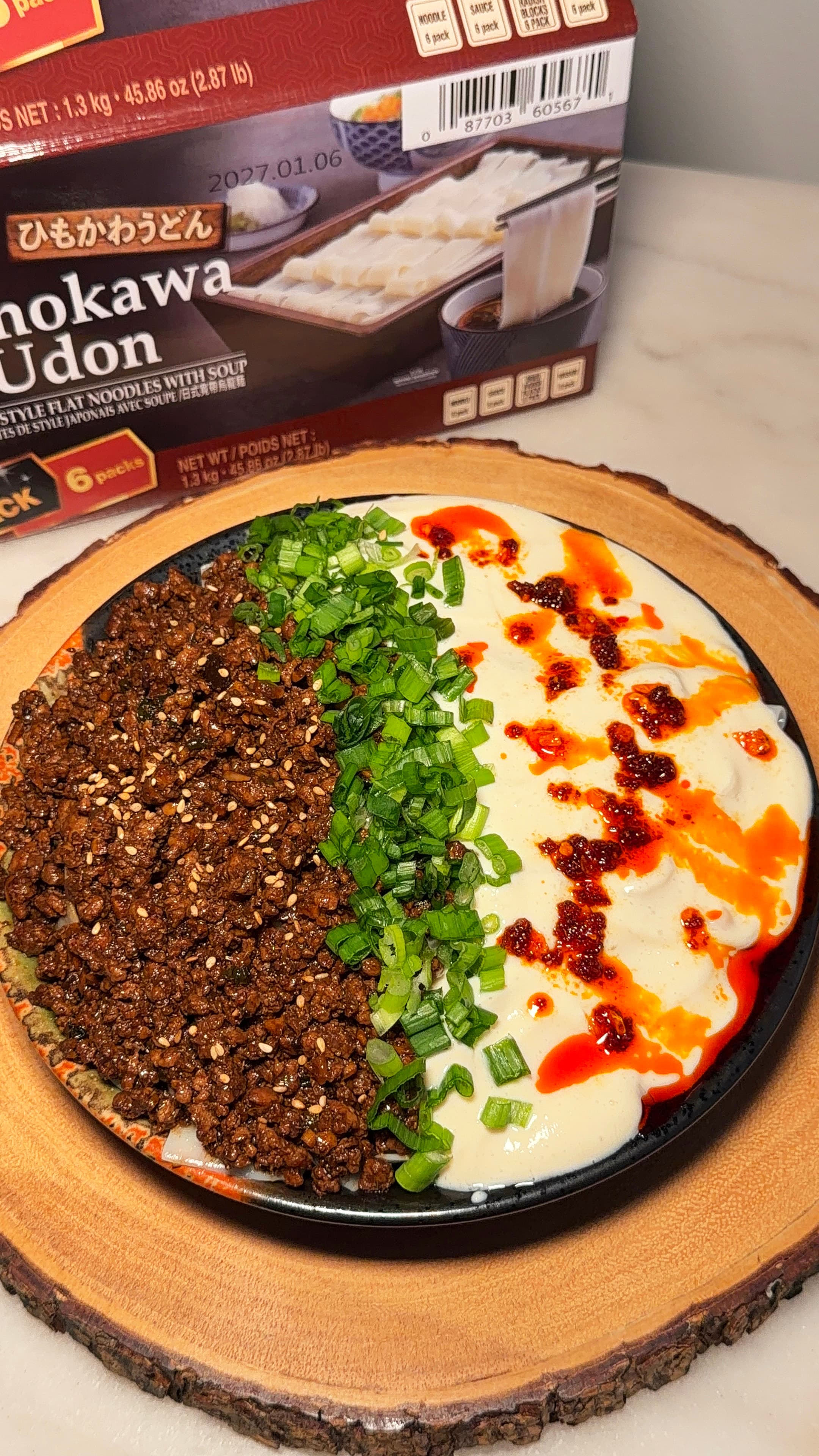 Flat udon noodles topped with spicy ground pork, silken tofu, green onions, sesame seeds, and chili oil