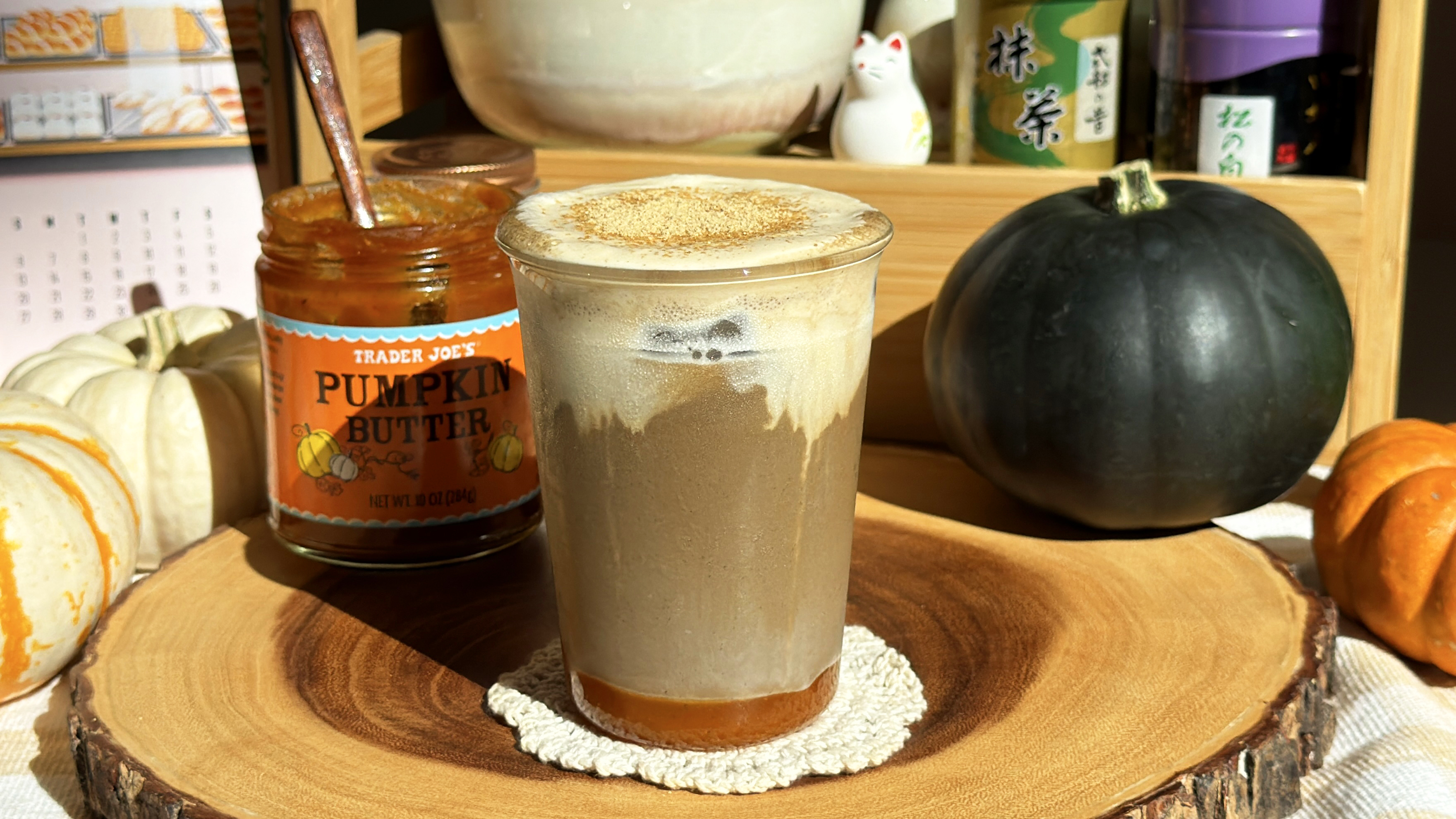 Iced kinako and pumpkin hojicha latte with a creamy top and kinako sprinkle, next to a jar of Trader Joe's pumpkin butter and a kabocha squash