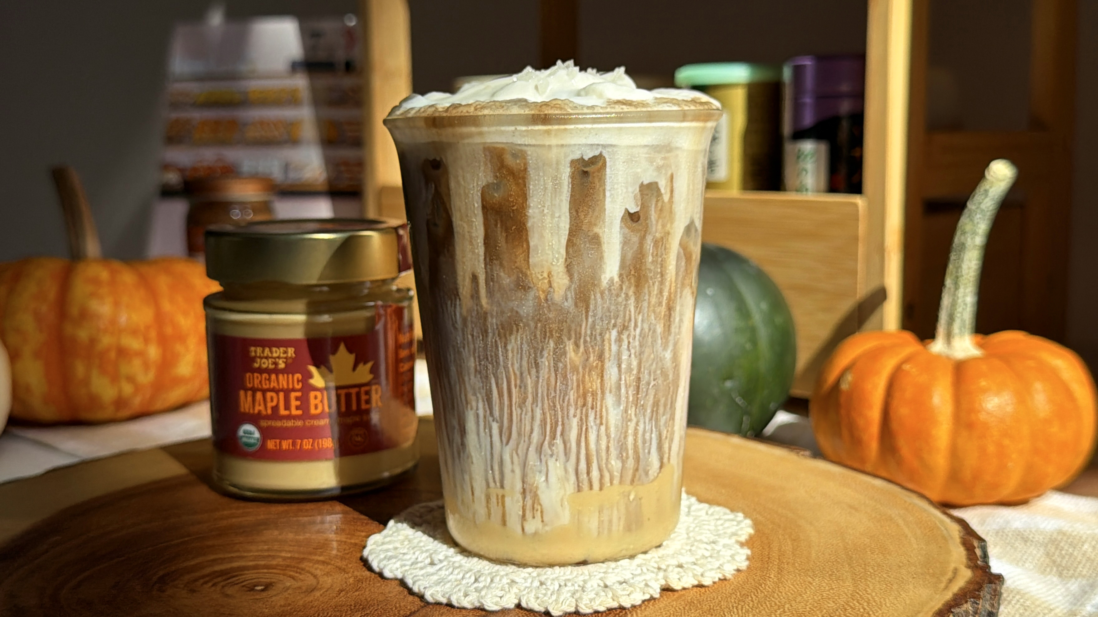 Iced hojicha latte with salted maple butter cream top, next to a jar of Trader Joe's organic maple butter and mini pumpkins