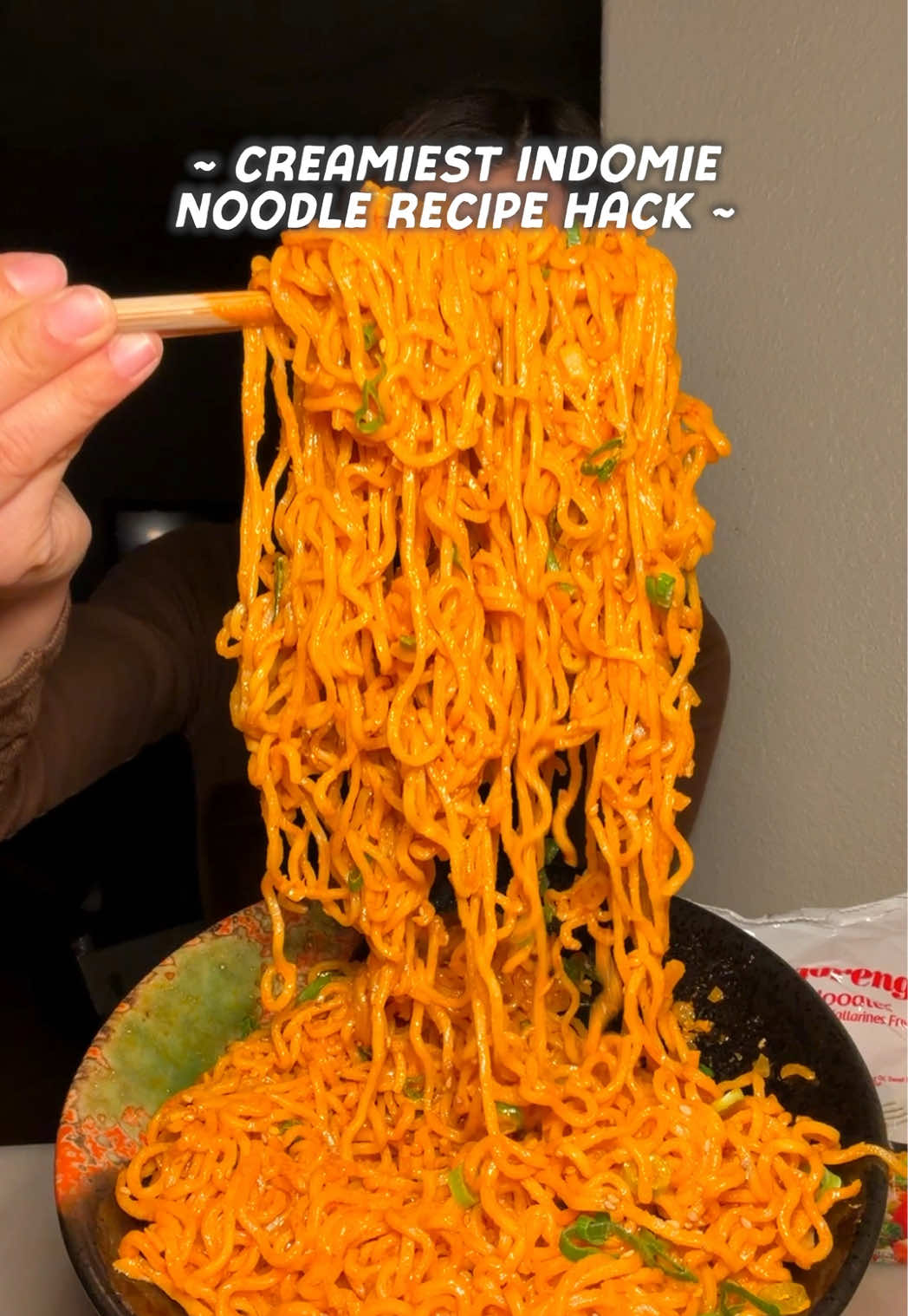 A creamy bowl of Indomie noodles topped with green onions and sesame seeds