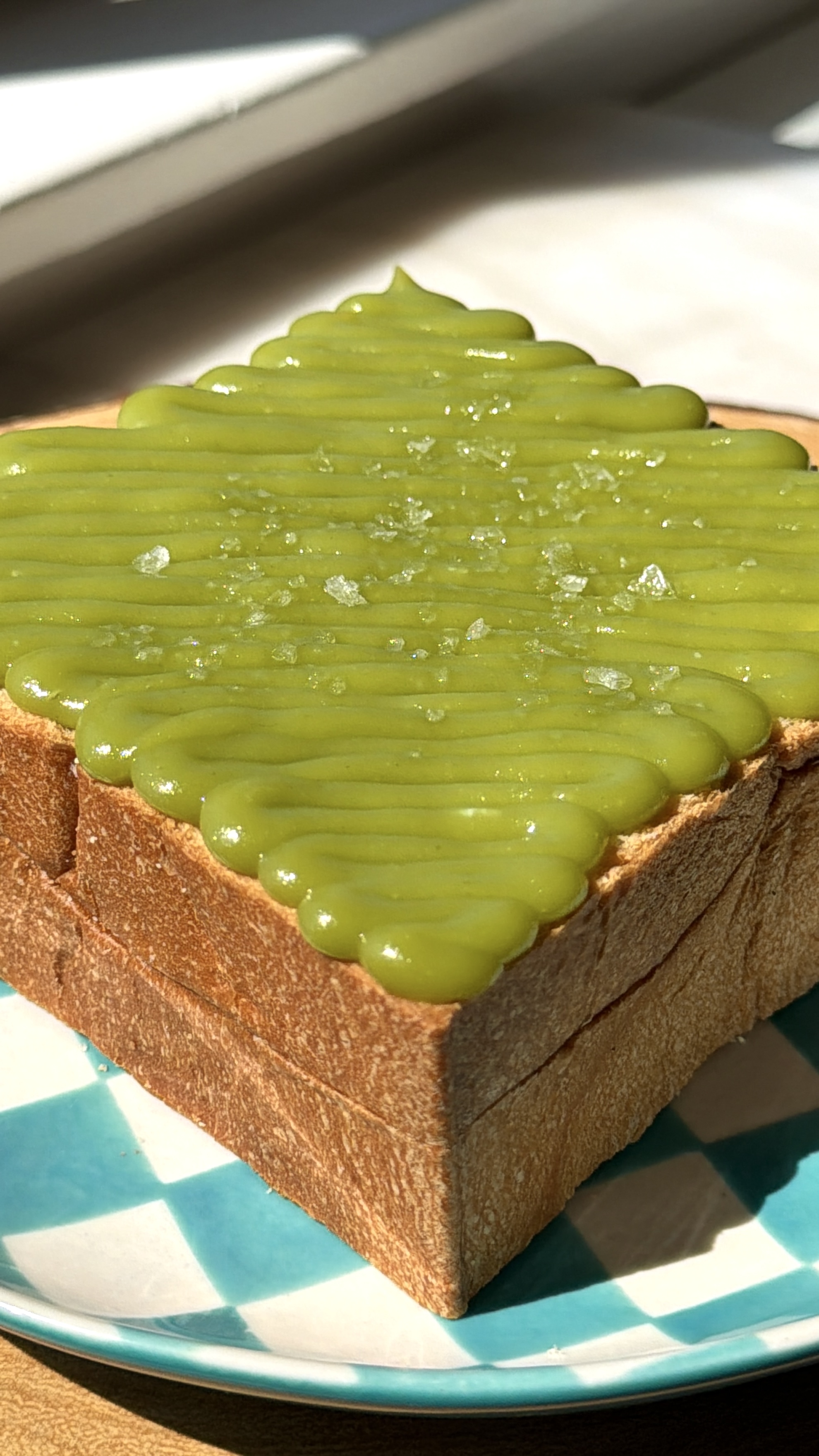 Angled view of Japanese milk bread topped with glossy pandan kaya custard and flaky salt in sunlight